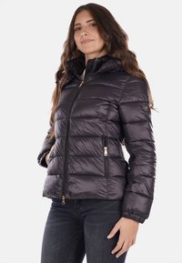 Giacca imbottita di colore grigio scuro con cappuccio, dotata di chiusura con zip, due tasche laterali e una texture liscia e lucida. Accentuata da dettagli in metallo dorato.