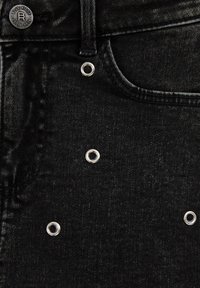 Črne jeans hlače iz denima s srebrnimi grometi, teksturirano tkanino in klasičnim dizajnom, ki vključuje običajno zapiranje na gumb in zanke za pas.