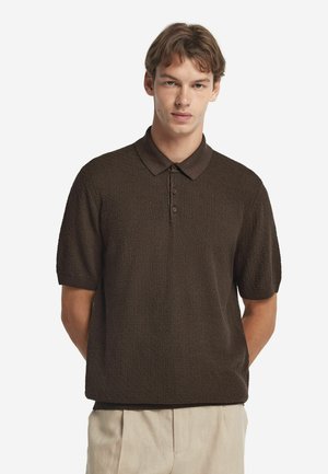 Braun strukturiertes Poloshirt mit kurzen Ärmeln, Kragen und einer Knopfleiste mit drei Knöpfen. Tragen mit hellen Hosen.