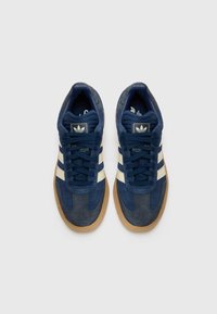 Zapatillas de ante navy con rayas blancas, punta redonda, acentos texturizados y suela de goma. Logo en blanco y negro en la lengua.