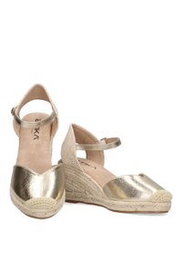 Sandalias de cuña cerradas en la parte delantera de metal dorado con correa en el tobillo, suela de yute trenzado y forro interior de color marrón claro. Superficie lisa con acabado brillante.