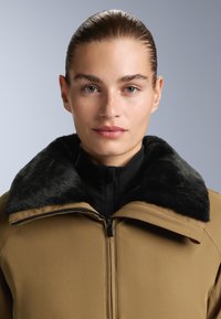 Brown outerwear jacket with a black faux fur collar, featuring a zip closure and smooth, textured fabric. Close-up view of collar and chest.