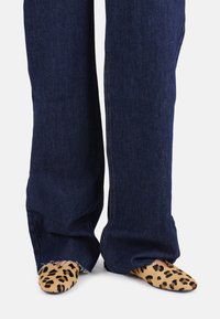 Jeans in denim a gamba larga di colore blu scuro con orli sfrangiati, abbinati a scarpe slip-on a punta in tonalità beige con un motivo a stampa leopardo nero.