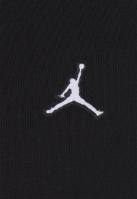 Silueta basketbalisty skákajícího s jednou rukou zvednutou a drženým míčem, vyšitá bílou barvou na černé látce.