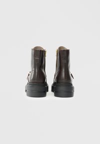 Bruine leren enkelbootjes met gouden ritsen, een stevige zwarte zool en gestikte details op een gladde bovenkant.