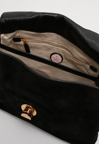 Wnętrze czarnej torebki z zamszu z beżową podszewką, wyposażone w kieszeń na zamek i zapięcie magnetyczne w złotym kolorze.