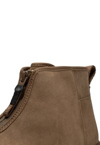 Bruine suède enkelboots met zijrits en trekstrip, met gedetailleerde stiksels en een gestructureerd oppervlak.