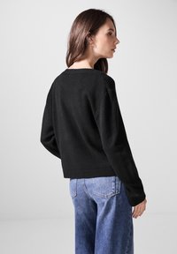 Schwarzer, strukturierter Pullover mit lockerer Passform, Rundhalsausschnitt und geripptem Saum. Kombiniert mit hellblauen, locker sitzenden Jeans.