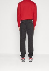 Röd sweatshirt med V-hals och långa ärmar, kombinerad med svarta byxor med elastiska muddar och fickor, bärs tillsammans med vita och röda sneakers.