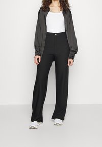 Svarta skräddarsydda byxor med hög midja, slät framsida och vida ben, tillsammans med en vit ärmlös topp och en mörk knäppskjorta.