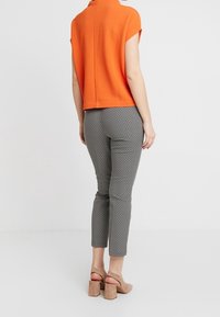 Oranžový top s krátkým rukávem a rozparkem na zadní straně, doplněný o černobílé vzorované skinny kalhoty a béžové sandály na blokovém podpatku.
