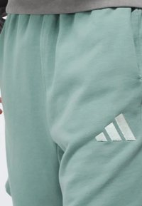 Lysegrøn sweatpants lavet af blødt stof med en elastisk talje og et sølvfarvet Adidas-logo på venstre lår.