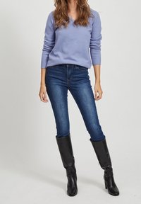 Jasnofioletowy sweter z dekoltem w serek, prążkowane mankiety; ciemnoniebieskie obcisłe dżinsy; czarne skórzane kozaki za kolano o dopasowanym kroju.
