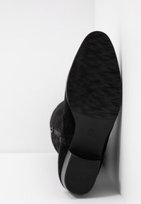 Czarne zamszowe botki za kostkę z teksturowaną gumową podeszwą, zamkiem bocznym i zwężanym kształtem. Spód ma gładkie wykończenie z subtelnym wzorem.