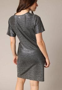 Robe brillante à manches courtes en tissu métallique de couleur gris foncé. Elle présente un décolleté rond et un détail discret dans le dos près du décolleté.