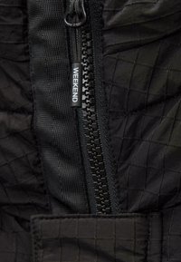 Schwarze Jacke aus strukturiertem Material mit einem Rautenmuster. Asymmetrischer Reißverschluss mit einem "WEEKEND"-Zipper und verstärkten Nähten.