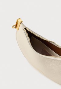 Crèmekleurig leren zakje met een gestructureerde afwerking, een ritssluiting met gouden beslag en een afgeronde vorm. De binnenkant is bruin met zichtbare merkaanduiding.