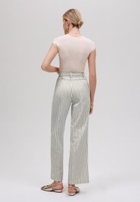 Lys beige ribbet topp, høyt liv på rette benbukser med vertikale grønne og hvite striper, sammen med nude sandaler.