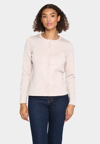 Cardigan rose clair à manches longues avec un col rond, fermeture à boutons sur le devant et texture côtelée, associé à un jean bleu foncé.