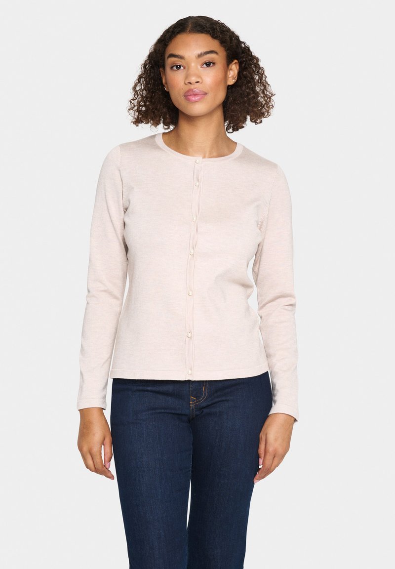 Cardigan rose clair à manches longues avec un col rond, fermeture à boutons sur le devant et texture côtelée, associé à un jean bleu foncé.
