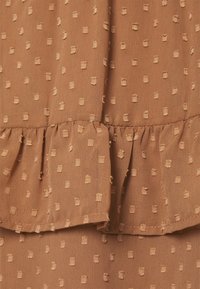 Tissu marron texturé avec un motif à pois en relief, doté d'un ourlet volanté et d'une finition lisse. Matière douce et légère.