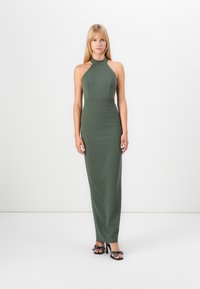 Olive green halter neck dress made of smooth fabric, fitted silhouette, floor length, paired with black sandals featuring decorative accents.