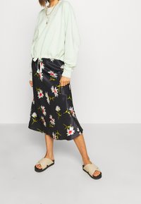 Mintgrön sweatshirt med dragsko i nederkant, kombinerad med en svart satängkjol med blommönster i vitt och rött. Beige slidesandaler.
