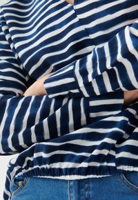 Blusa a righe blu navy e bianca con scollo a V, maniche lunghe e orlo arricciato, caratterizzata da una texture liscia e polsini con bottoni.