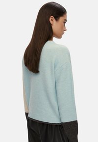 Maglione azzurro chiaro con una vestibilità comoda, caratterizzato da maniche beige e grigio scuro a contrasto. Texture morbida e dettaglio a costine sull'orlo.