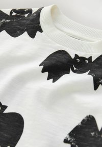 Camiseta de tela blanca con un patrón de murciélagos en negro. Cuello redondo con borde acanalado y superficie suave, ligeramente texturada.
