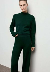 Suéter de punto verde oscuro con cuello alto y corte holgado, combinado con pantalones de pierna ancha de talle alto a juego, ambos hechos de material suave.