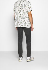 Kortärmad vit skjorta med gröna växtmönster, tillsammans med mörkgrå jeans och grå-vita sneakers med gula accenter.