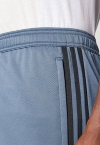 Blå atletiske shorts lavet af glat stof, med et sort stribedesign på siden og en elastisk talje.