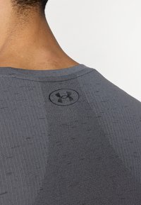 Γκρι αθλητική μπλούζα με υφή υφάσματος που διαθέτει κάθετα και οριζόντια μοτίβα. Περιλαμβάνει μαύρο λογότυπο κοντά στη λαιμόκοψη.