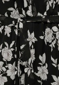 Black floral dress fabric featuring large white flowers and leaves. Fabric has a lightweight, sheer texture with a tied waist detail.