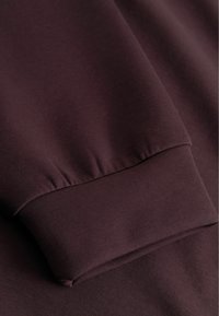 Tumed pruun fliis, millel on sile tekstuur, elastsete detailidega kokku gathered mansett, lähedalt kaetud pilt, mis keskendub varrukaele.