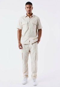 Lys beige kortærmet skjorte med to brystlommer, parret med matchende cargobukser med sidelommer. Båret med hvide sneakers.