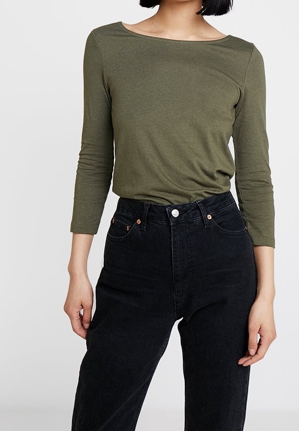 Maglietta aderente a maniche lunghe verde oliva con scollatura ampia, abbinata a jeans neri a vita alta con dettagli in rame e cinque tasche.