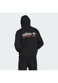 Juoda sportinė palaidinė su gobtuvu, ant kurios nugaros yra baltu ir koraliniu spalvomis užrašyti "adidas" ir "ADVENTURE". Pagaminta iš minkštos, tekstūruotos medžiagos.
