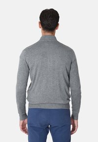 Maglione grigio lavorato a maglia con collo alto, polsini e orlo a costine, abbinato a pantaloni blu. Nessun motivo visibile o dettagli in metallo.