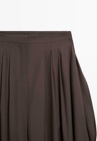 Pantalon marron taille haute à jambes larges avec plis et fermeture avant cachée, présenté sur fond blanc.