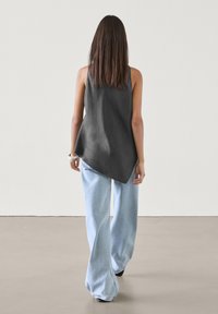 Szara bezrękawnik o swobodnym fasonie, w połączeniu z jasnoniebieskimi spodniami typu wide-leg. Gładka tkanina o luźnym kroju i asymetrycznym dołem.