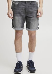 Grå denimshorts med lys fading, oppbrettede ermer, fem lommer og et gullmerke på midjen, kombinert med hvite sokker og marineblå sneakers.