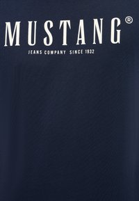 Granatowa bawełniana koszulka z dużym białym napisem "MUSTANG JEANS COMPANY SINCE 1932" z przodu. Miękka tekstura, klasyczny krój z okrągłym dekoltem.
