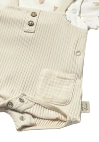 Romper de bebé color marfil con textura acanalada, dos botones y un bolsillo. Tiene cierres a presión en la parte inferior para facilitar el cambio de ropa.