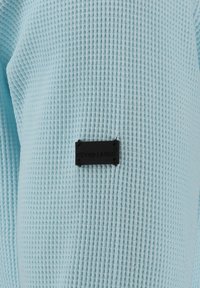Camicia di un blu chiaro con texture, caratterizzata da un motivo a maglia waffle e un piccolo etichetta rettangolare nera con la scritta "KEY LARGO" in rilievo.