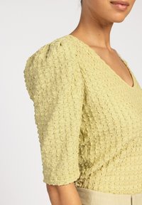 Lichtgele blouse met textuur, korte pofmouwen en een V-hals, met een geweven patroon voor extra dimensie.