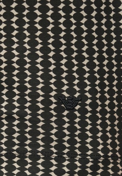 Čierna a béžová tkanina s geometrickým vzorom striedajúcich sa kruhov a tvarov. V dolnom rohu je malá vyšívaná značka.