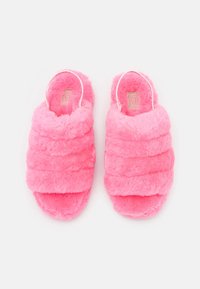 Para jasnoróżowych, puszystych klapek z otwartym palcem, z pikowanym wzorem i metką UGG wewnątrz, wyeksponowanych na białym tle.