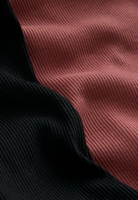 Gros plan d'un tissu côtelé avec des sections alternées de noir foncé et de rose atténué, montrant la texture et des plis doux.
